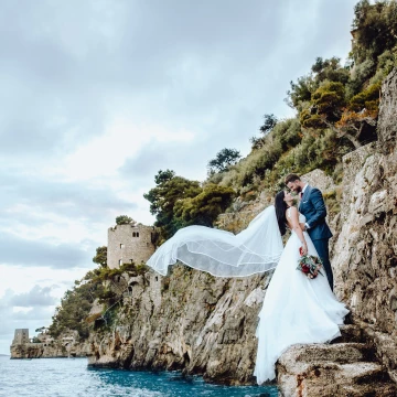 This image was taken in Positano, Italy. We wanted to show the dress and veil in all the glory, that why the couple stands on this small edge.