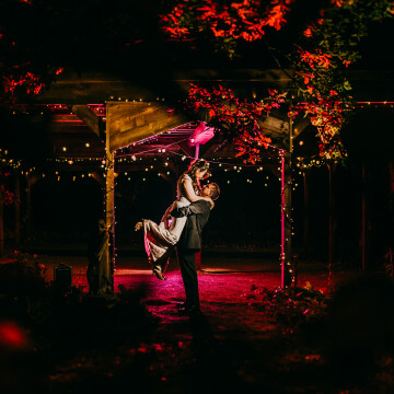 I created this shot using 3 lights. A key light to light the couple. A purple gelled flash further back and a red gelled flash. They all work to create a lovely photo. I asked the groom to give the bride a lift to add something dynamic and it works well.