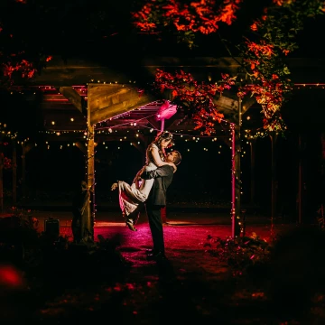 I created this shot using 3 lights. A key light to light the couple. A purple gelled flash further back and a red gelled flash. They all work to create a lovely photo. I asked the groom to give the bride a lift to add something dynamic and it works well.