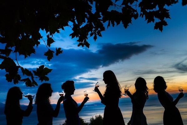 This wedding took place at one of the  most beautiful places I've been to, a Unesco protected place called Lavaux in the Swiss-French region. The reception was in the middle of the vineyards with amazing views of the lake. My client, who invited all her fun girlfriends from Mexico asked me for a group photo with her friends. This photo was a non-literal & creative interpretation of their fun gathering, in that particular place and atmosphere. It was sunset time, I could have lighted the scene completely but then the image would have lost impact. Our eyes are not used to seeing this way so it makes us feel curious about the scene. I could have taken a simple and boring group photo. However, I wanted to show the reason why they chose this venue for their wedding, which was the great wine from that region, the views and the fun company.