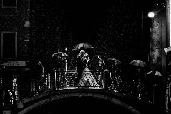 During trash the dress session in Venice it started to rain. Under an umbrella grooms they stood over a bridge while passers crossed it from one side to the other.