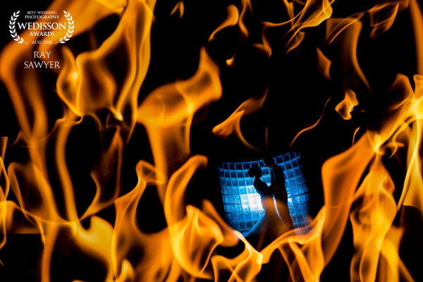 Having took 6-7 photos of some flames from a fire I then captured a shot of the couple in the semi circle glass wall and used the in camera double exposure feature to create the final image.