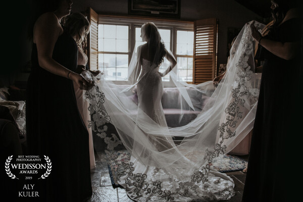 I didn't plan for this shot. I always shoot what my eyes see. Ashley was all ready to go for the ceremony and the bridesmaids started to pick up her dress. This moment I saw how the texture of the gorgeous veil and the lighting coming out from the window into that dark room to give a dramatic look en mood to this image. 