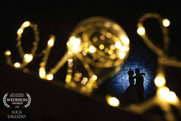 This picture was taken at the wedding of Angela and Manuel, in Italy at Garda lake. It was taken with an off-camera flash with a blue filter, pointed on the wall behind the couple to make the right color contrast between the love write and the silhouette of them. I'm really proud of this image.