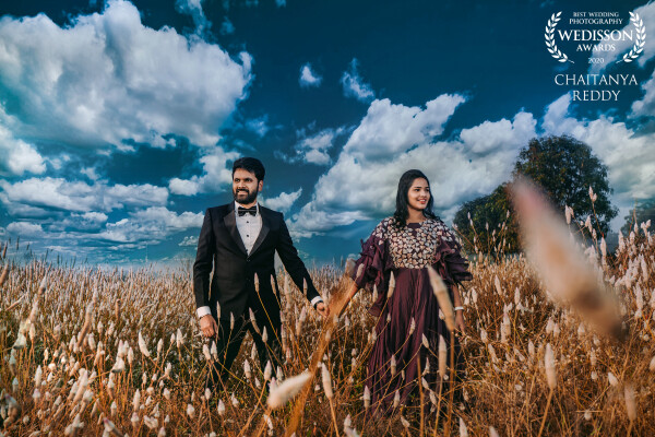 As our shoot was planned earlier, I and my team on a full swing reached the location. It was an early morning shoot looking at those fast-moving clouds, I had an idea of taking a click of the couple in that beautiful cloudy atmosphere. And I wished no rain would spoil my idea. And in a Hurry, when I took my weapon to click a beautiful picture as expected; The clouds in the sky, the grass on the ground, the couple in love gave me an amazing picture. Which was really a memorable picture that was composed by me. And I name it, “A touched Feel of Love”