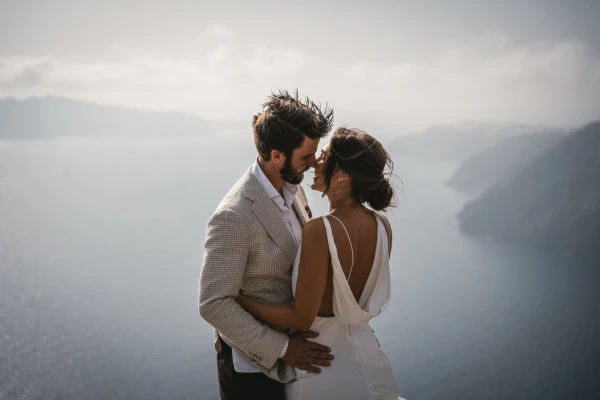 Perched high above the azure waters of the Aegean Sea, this couple enjoys a breathtaking moment duri...