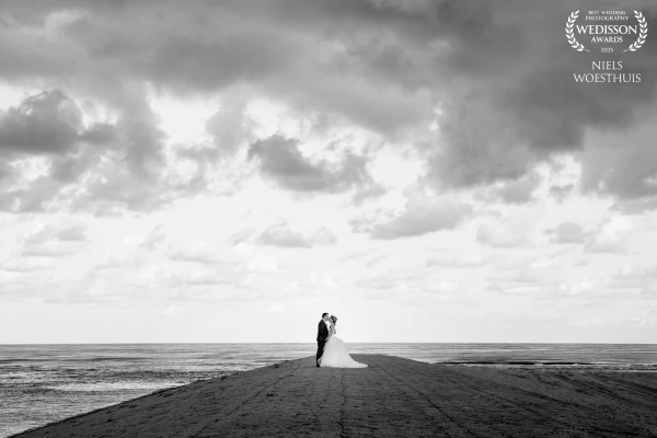 A striking black-and-white capture of a couple embracing at Katwijk aan Zee, set against dramatic cl...