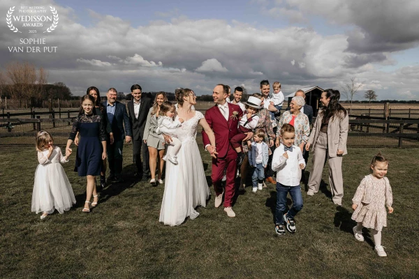 A wedding group photo filled with love and motion, captured in the fleeting moment when sunlight pie...