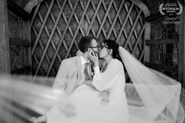 A soft, emotional moment tucked away under a wooden arch, Anya and Moby share a kiss as her delicate veil sweeps through the frame.