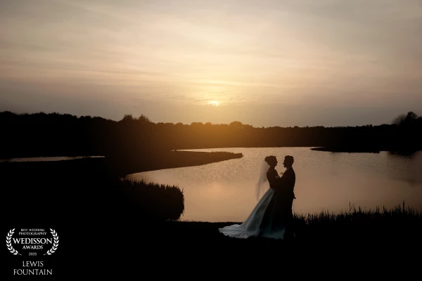 A romantic sunset silhouette by the lake, capturing a quiet, intimate moment between Becky and James as the sun was setting at The Old Hall Ely.
