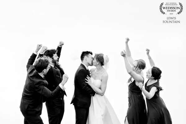 Becky and James having a kiss while their wedding party cheer them on. This shot was actually taken from above and into a lake, which gave the effect of a bright white sky. A bit of a fun shot from their day at The Old Hall Ely.