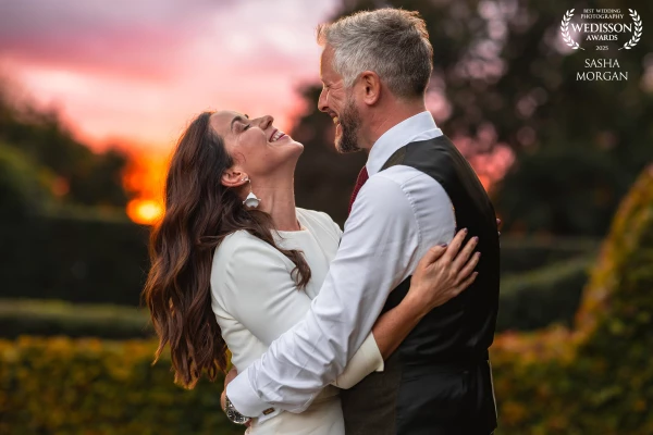 A couple share a warm, genuine moment as they laugh together during a beautiful October sunset. The...