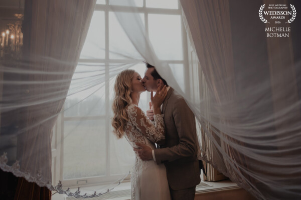A quiet, intimate moment: a beautiful bride and groom under her veil by the window of a stunning cou...