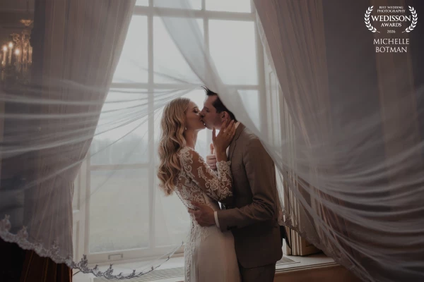 A quiet, intimate moment: a beautiful bride and groom under her veil by the window of a stunning cou...