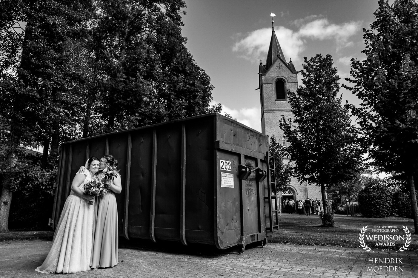This picture is pure storytelling to me and I'm always thrilled when something like this happens on a wedding day. The bride hides with one of her bridesmades behind a huge dumpster while the whole wedding party is entering  the church. She's quite nervous and nobody saw her standing there. Such a special moment!