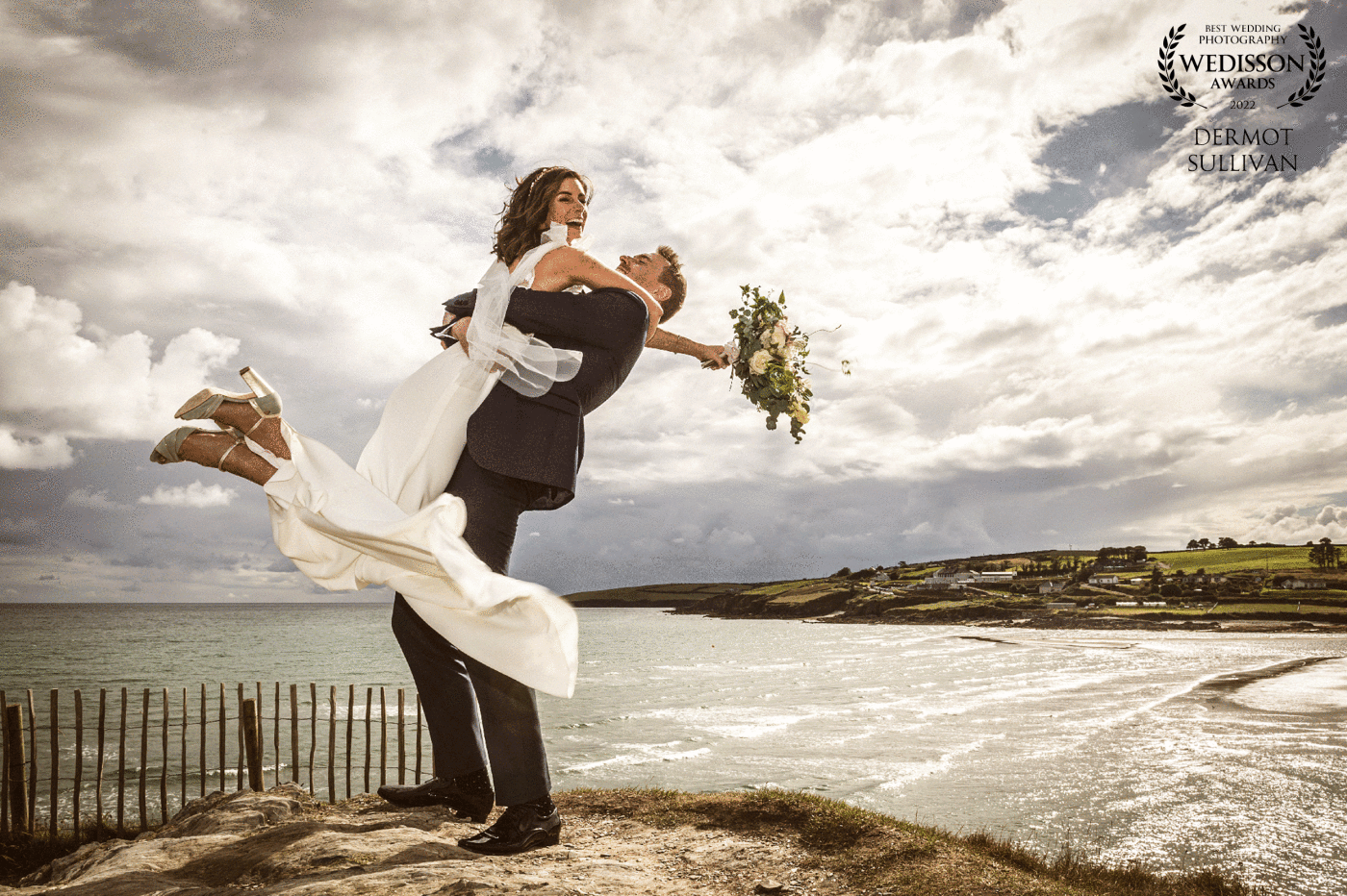 This photograph was taken on a headland overlooking the sea at Inchydoney, in West Cork, Ireland. The couple are pretty sporty and the groom + his party had already been for a swim in the Atlantic earlier that day. We had done some more static shots and then I asked the groom if he could lift his bride up for a more dramatic shot. I went low to capture her against the sky and I added some fill in flash at +3 power so that I could get some detail in the sky.