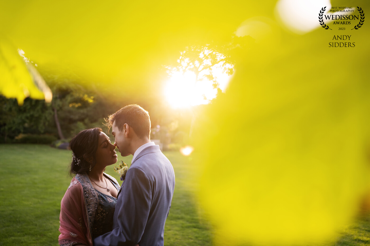 This romantic shot was captured at The Barns at Redcoats in Hertfordshire, UK. The couple were backlit by the golden hour sun and I shot through leaves to create the yellow/green-ish bokeh in the foreground.
