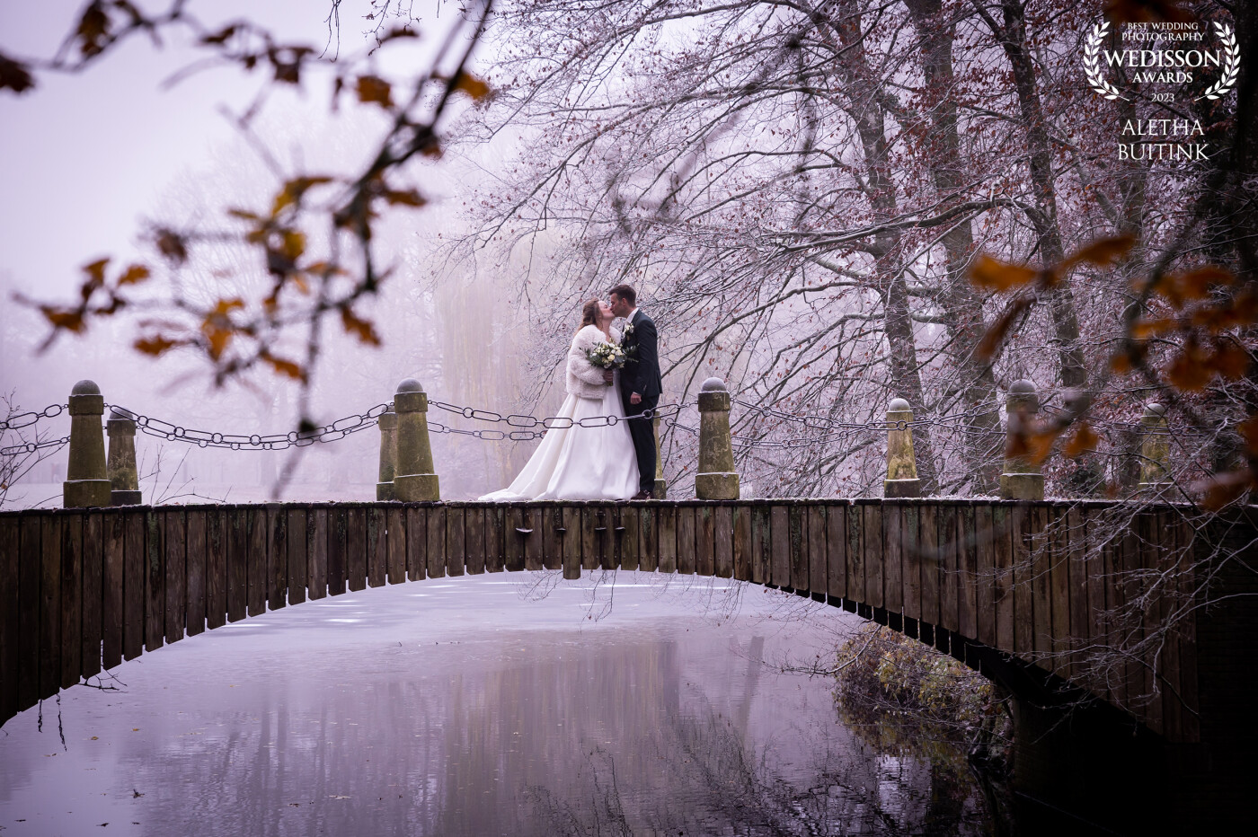 The 10th of December it was icy cold. The photoshoot took place at a nearby forest and right at the beginning was this beautiful bridge. As soon as I saw this I knew this photo had to be taken. The red-brown leaves against the icy sky created a wonderful mysterious atmosphere and the kissing bridal couple completed the picture.