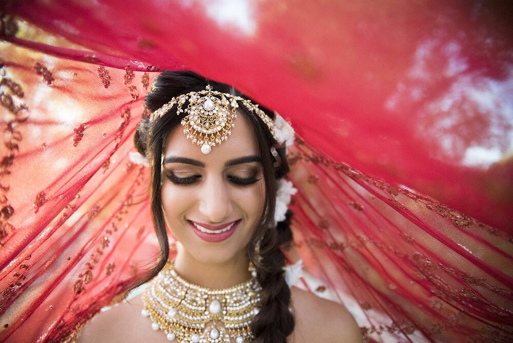 Indian Weddings are all about colour and lots of it! ​ This bride is wearing a traditional Indian Lengha in the colour palette of the year, Marsala. With Jewels, Indian brides are covered in everything from toe rings, to hand pieces to layers of necklace and headpieces. Our bride is wearing a choker necklace with a waterfall draped longer piece. <br />
A headpiece that fits like a crown with a centre bindi piece. The makeup stylist, Toby Wesenberg used bold earth tones with golds and brown to enhance this beautiful bride. Her lips were coloured in a burgundy to bring the look together. The hair style was a unique side braid with white flowers by Blue Sage Farm - Floral Design to bring this bride up to par in tradition and elegance. The wedding took place in Okanagan, BC. a destination location for brides of all sorts. The Okanagan Valley is known for top location to say "I do".