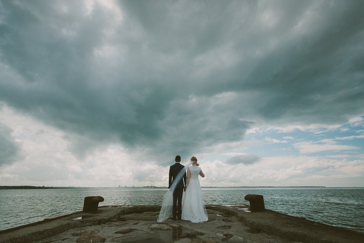 This was shot on the way to the wedding venue, on a pier in Pirita, Tallinn, Estonia. We knew beforehand that the couple wanted a few shots there, with the view to the city. What I could not have hoped for was the dramatic sky that afternoon.<br />
At some point during the Big Day of each couple there is a moment they relax, stop worrying about the small things, and just ride the wave of the wedding day.<br />
I guess the importance of that shot for Pavel & Jekaterina, besides the view itself, is that after we left the pier for the venue, that moment had arrived. And Jekaterina walked down the aisle alongside his father with a big smile
