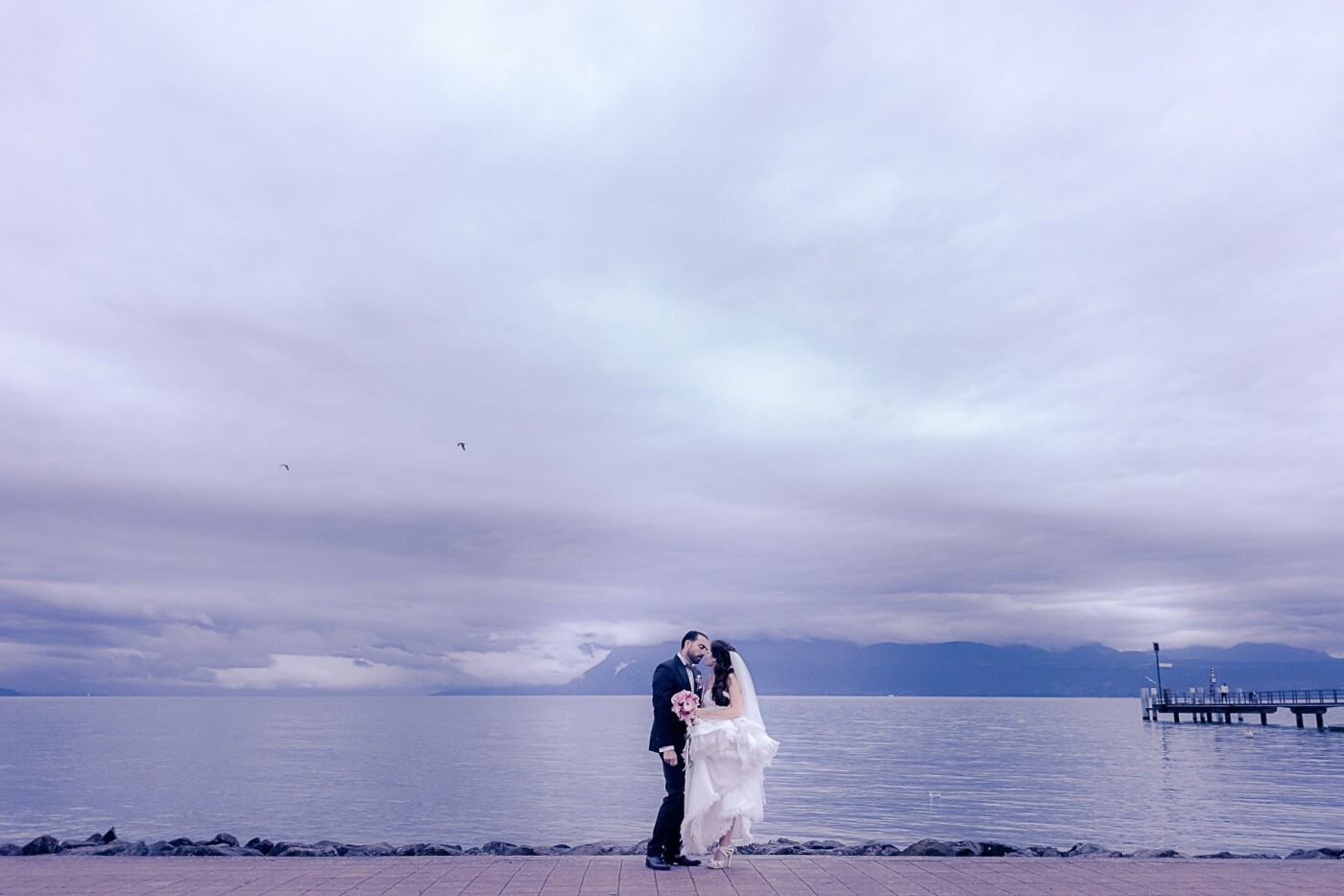 I can’t think of a single bride on earth who wouldn’t get a little nervous in prospect of a rainy day wedding. But who said rainy day weddings photographs can’t be just as intense as the idyllic blue skies shots? Passion doesn't fear bad weather, nor does creativity.<br />
As the ceremony ended, the skies above the Leman Lake (or Lake Geneva, Switzerland) started to get darker and darker, until it literally started pouring with rain. I could see the disappointment on the bride and groom’s faces. But their love, their happiness and the infinite beauty of that day were way above the quirks of nature.<br />
As the rain calmed down, the panorama revealed its magic. The skies were as dramatic and the couple’s look at each other. The clouds were as soft and ruffled as the bride’s dress when she held it above the floor. The lake and the mountains were as mysterious and intense as the million feelings that seemed to run through the bride and groom’s bodies and souls.<br />
Soulmates. That’s all I can think of.
