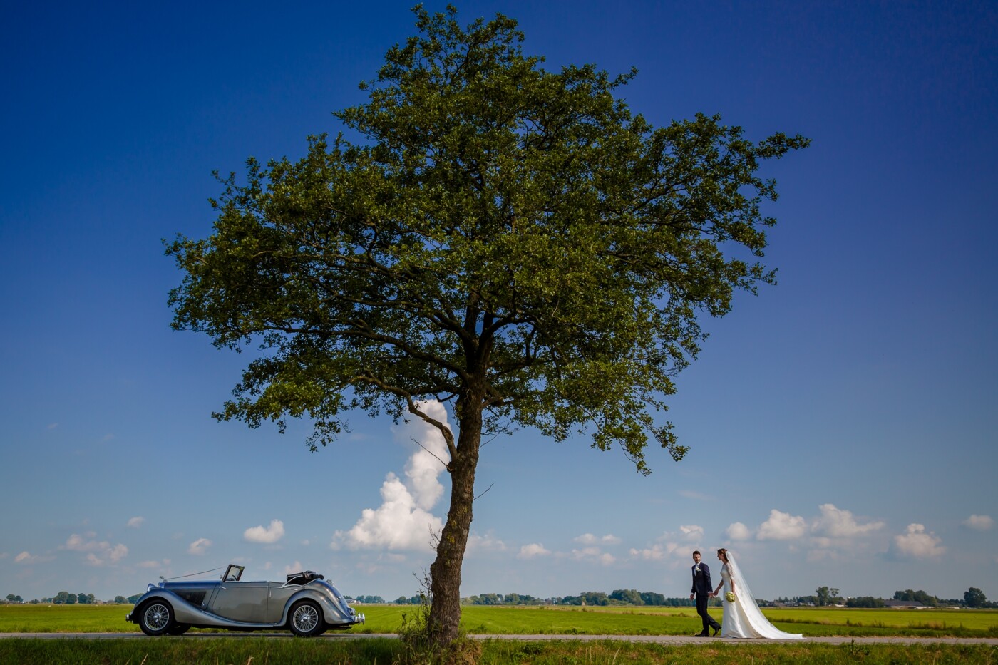 I am a big fan of black and white pictures. But when I pressed the shutter, I already knew that I wouldn't edit this picture in black and white. The great blue sky on a sunny summer morning. The beautiful lonely green tree. The classic cabriolet and ... the stunning wedding couple. A great mix of colors and elements.