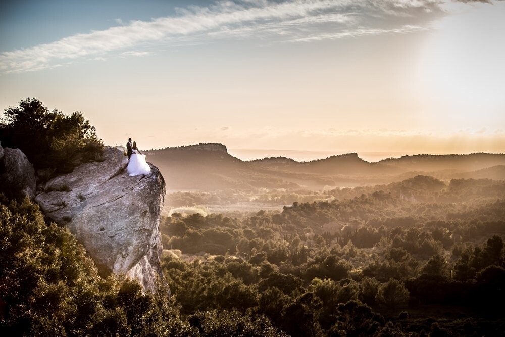 This picture  has been realized in South of France on the rock near « Les Baux de Provence ». I wanted a photo overlooking the valley during the sunset. This rock was great but to get there, the couple had to pass between 2 smalls rocks and spanning a hole 12 meters high !  My very brave honeymooners achieve this feat for to have this picture.