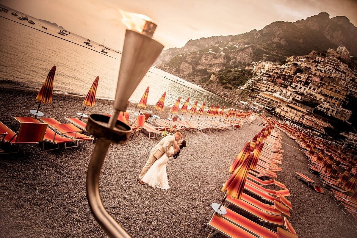 While photographing a wedding in Positano, Italy I was walking along the beach looking for the perfect place to get a wide angle shot. I wanted to showcase the beauty surrounding us, but I was looking for something special to make the photo a little more unique.  Across the beach, I came across a cliff with beautiful flaming lanterns that were hanging from the side of it. I told the couple to remain on the beach as I climbed the side of the wall to get my shot. It was exactly what I wanted.