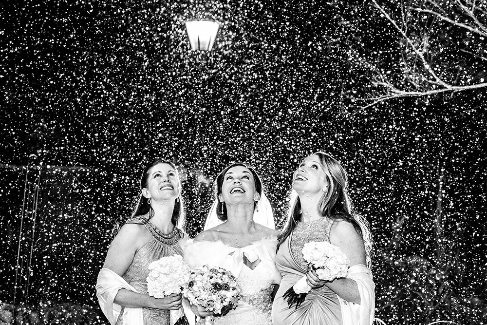 This was just after the ceremony had ended and I was taking family portraits with the bride and her family. Out of nowhere the sky just started dumping snow, and a lot of it. The bride happened to be standing next to her sister as well as her new husband's sister when it started, and right away I motioned for my assistant, who was holding an off camera light, to jump behind them and she understood right away. What I was able to capture was a pretty awesome moment when the first snow started to fall.