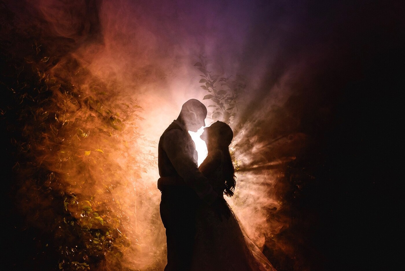 This photograph was taken at Sandhole Oak Barn in Cheshire, UK. The couple are lit by a single gelled speedlight placed behind them and I also set off a smoke bomb behind the couple, in front of the flash, to make the photograph look more dynamic.