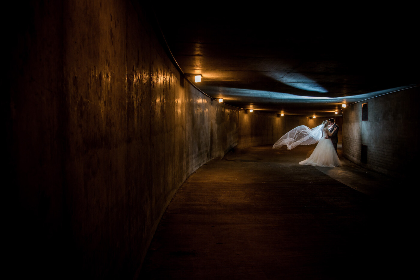 This shot is from the wedding day of Jaye + Dave, they were married in October. The shot is captured in an underground tunnel leading to a car park. Our couple were tired as this shot was at the end of their location photography on their wedding day. We quickly set up a couple of flashes and our couple quickly got in place. One of us then flicked the bride's veil up and ran out of shot whilst the other took the shot. We're really happy with this image, as is our bride and groom. We were lucky too, a security guard came to tell us to move on just as we'd captured this one. 