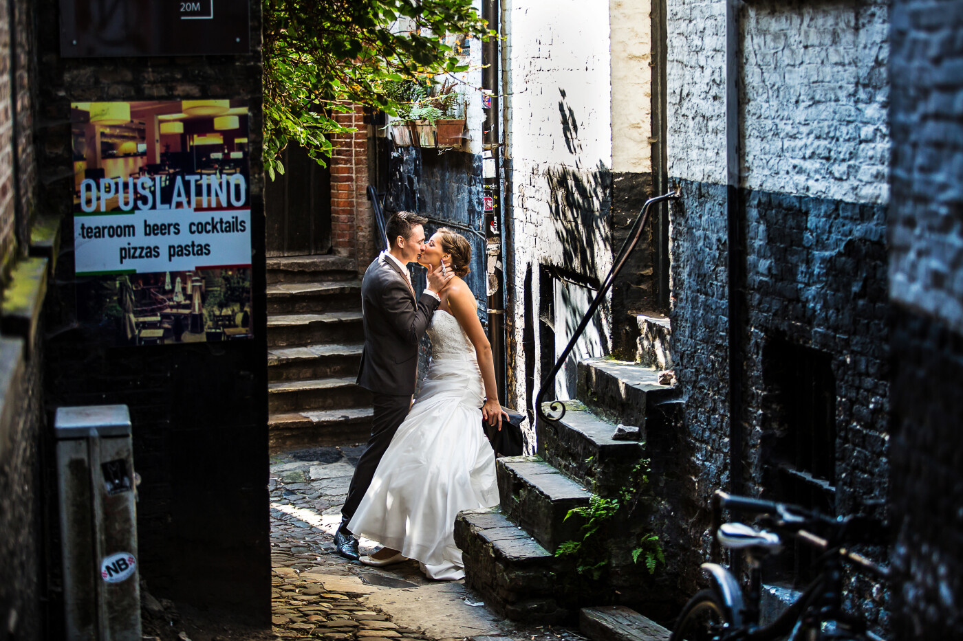 August 27th, 2016, Bruges. It was an extremely hot day in Belgium! The photoshoot of this young couple was in the center of Bruges. In the historical center, you can discover innumerable amazing places after every corner, a true gift for a wedding photographer. <br />
This shot was taken in a very small alley, in front of an medieval little factory, nowadays a cosy tavern.<br />
Despite the bright light on this very sunny day, the light in the alley was subtle and gave the picture an intimate atmosphere.