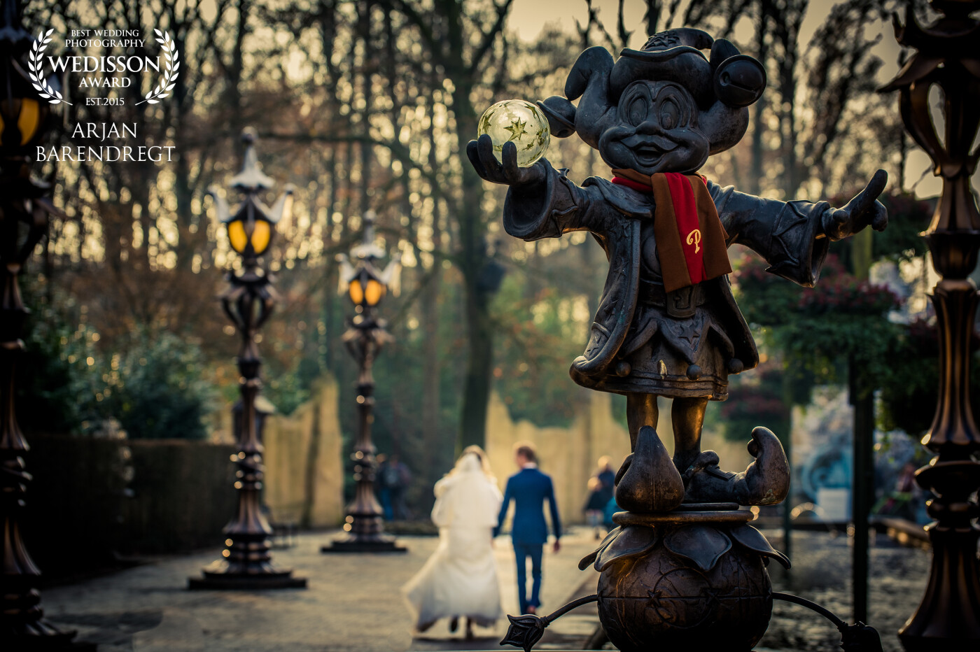 This photo is taken in attraction park De Efteling during their special winter theme.<br />
The bride and groom were walking back to the exit of the park, perfectly in the winter sun.<br />
On the foreground we see the mascot of this park, Pardoes.