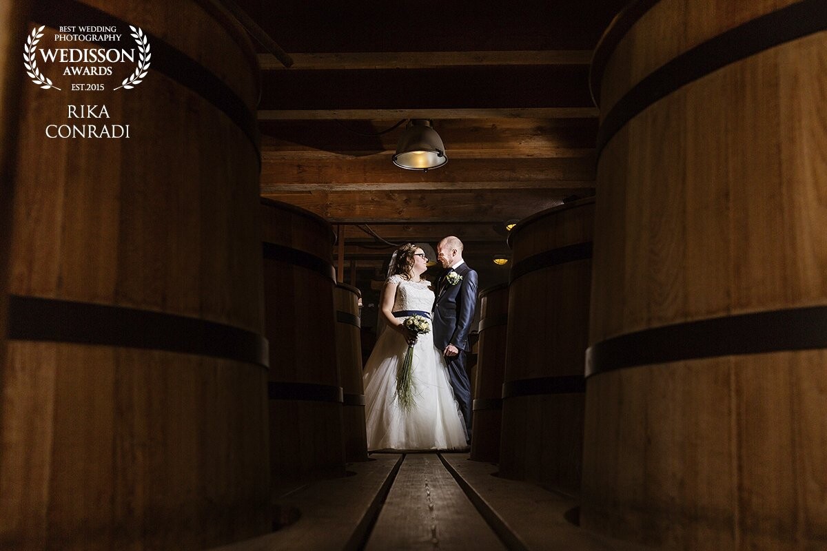 This couple wanted to marry at a historic place. It became the Jenevermuseum in Schiedam, Netherlands. I just developed myself into the off camera flash skills, so this was my first wedding where I put it to work. <br />
Between the barrels, with the smell of fresh brewed jenever, this bride and groom looked at each other with so much love. It was a moment away from the ceremony, which took place upstairs. 