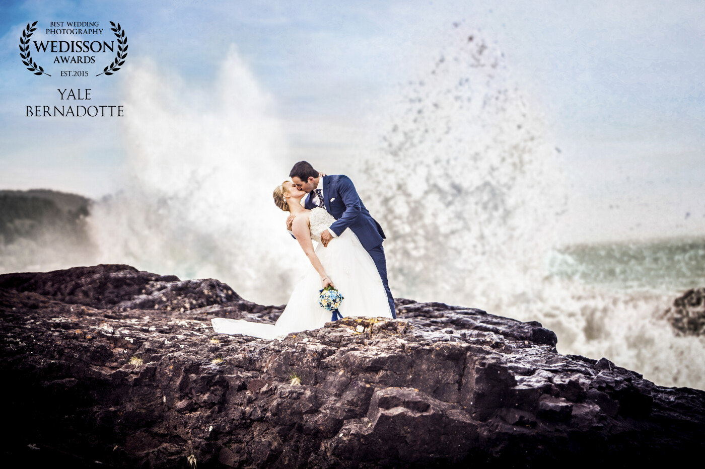 The north shores of Lake Superior are dramatic and breathtaking, constantly showing its' power and beauty. So when the opportunity came to capture this wedding I was excited at the challenge. <br />
<br />
I saw a rock formation jettisoning out from the shoreline and given the wind that was churning up the waters, knew this was the spot for something amazing. I had the couple carefully place themselves as close to the action as possible without putting themselves in too much danger. They knew they would get wet but were excited to hopefully capture the photo I hoped to take. <br />
<br />
I told them that once in place, they needed to hold their pose until I said so as I needed just the right wave sequence to come in. After much patience on their part, the perfect wave hit and this was the result.  