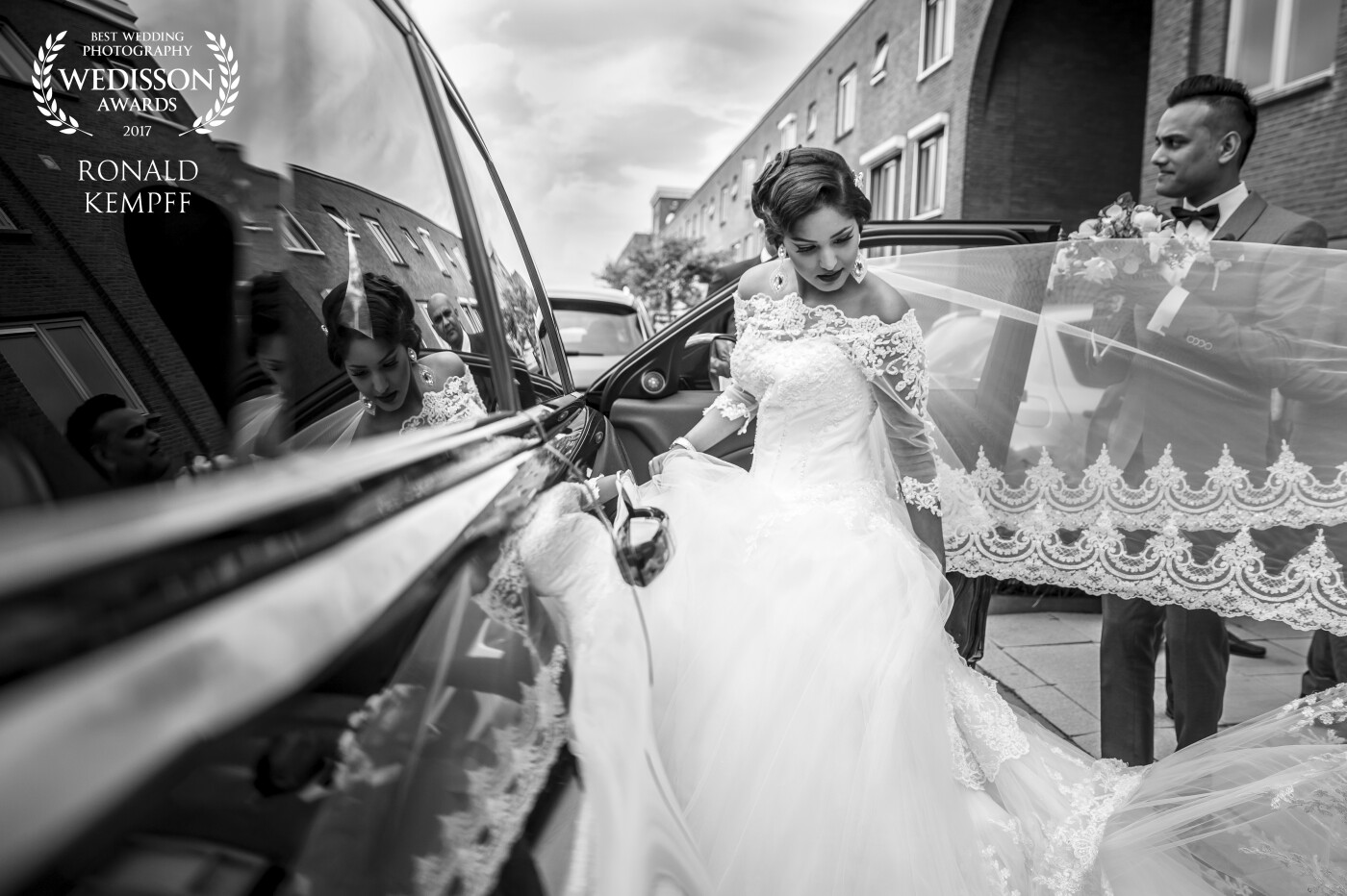 The picture was taken in front of the bride's house. At the moment she walked to the car, I saw her reflection in the car and knew that it would be a nice picture. At this moment she was preparing to get in the car, while the groom was waiting for her to get in.