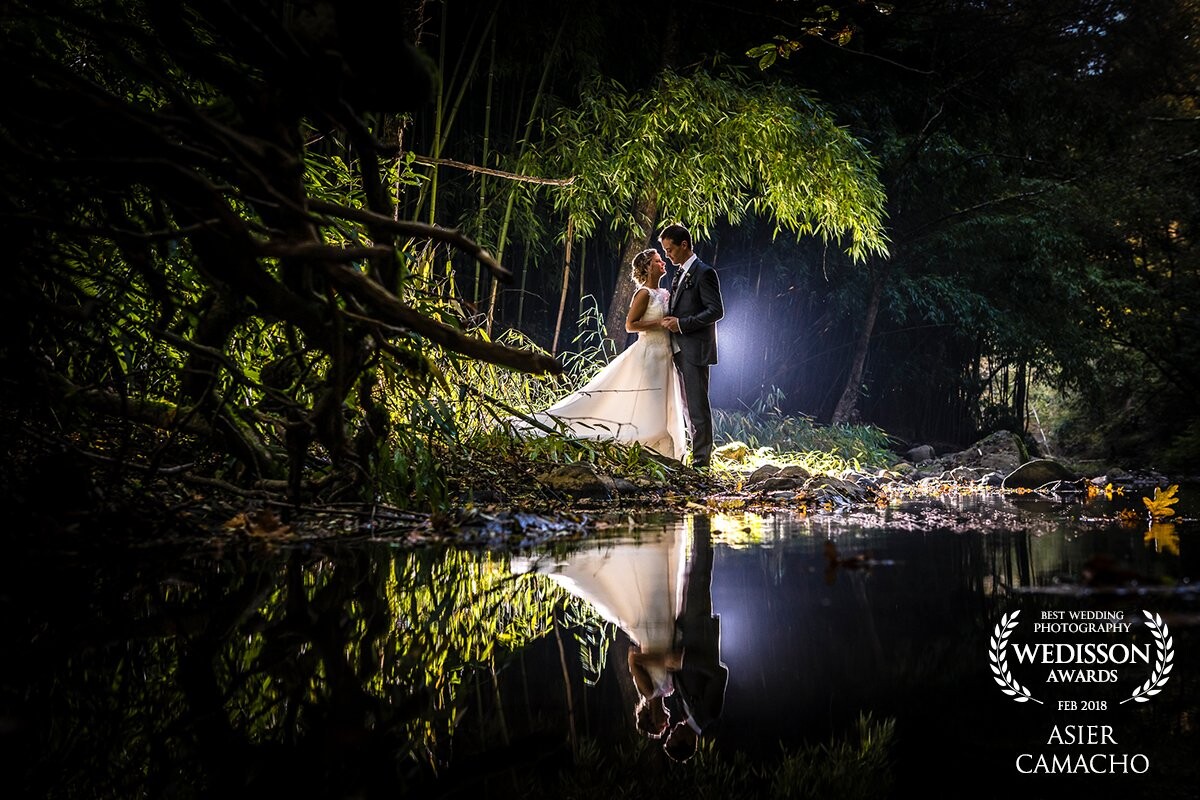 Photography taken during the day in Bizkaia, Spain in a place called "ferreria museum", behind the couple there is a 600w flash remotely controlled to create a dark atmosphere arruando the groom and bride. the camera is very close to the water to create a clear reflection of them.