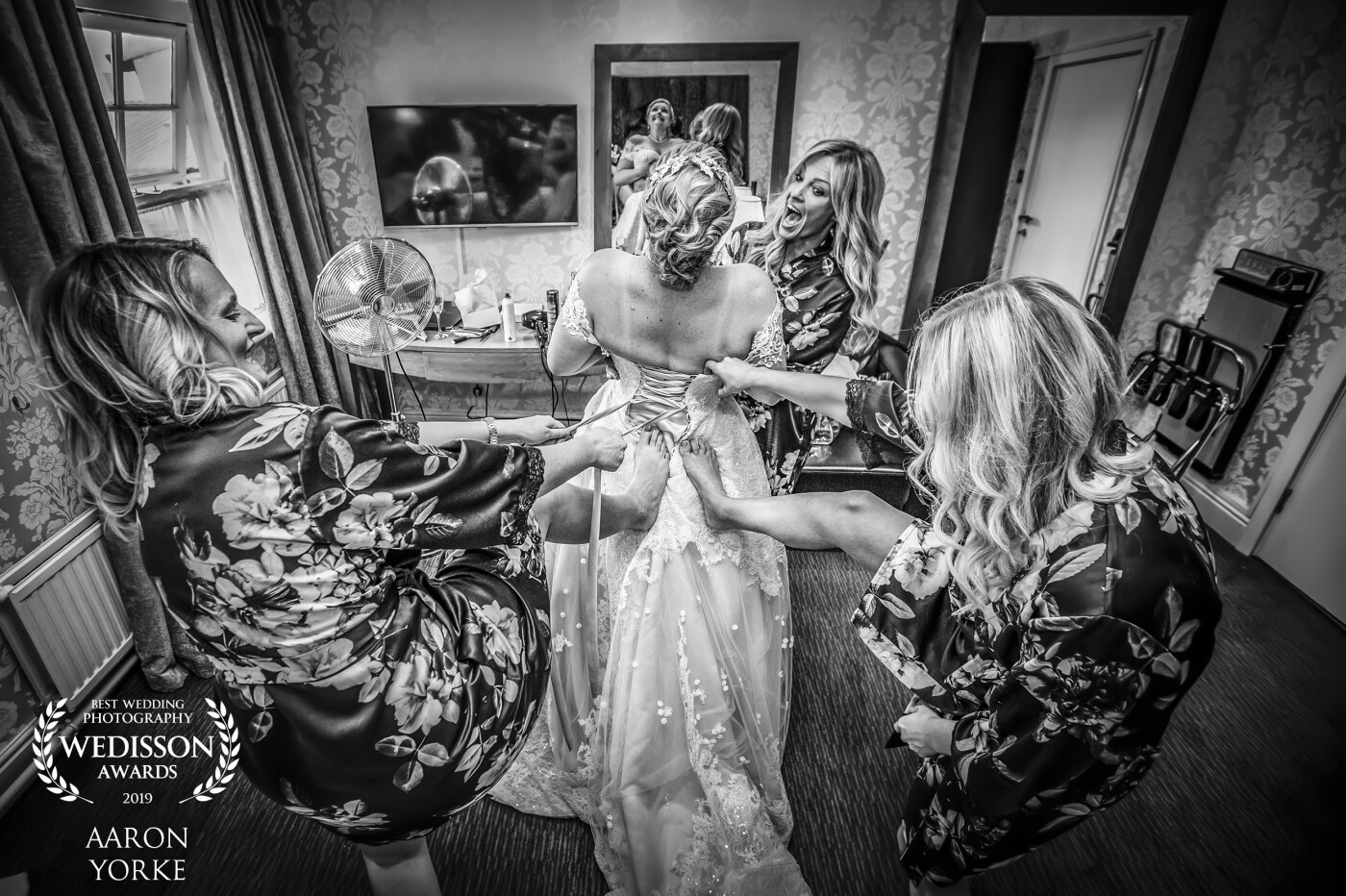 This image was taken at the Solihull Regency Hotel, Solihull UK. To get the shot I stood on the bed as the bridesmaids help the bride to put her dress on. I wanted to get a shot that showed the fun side to fit into a wedding dress, as the bride wanted to make sure she fitted into hers perfectly!! I angled the camera down from above to create the leaning back effect and set the lens to its widest (16mm) My camera gear was a Canon 5D, 16-35mm 2.8 lens ad f28, 1-100, on camera flash with a magmod bounce diffuser. 