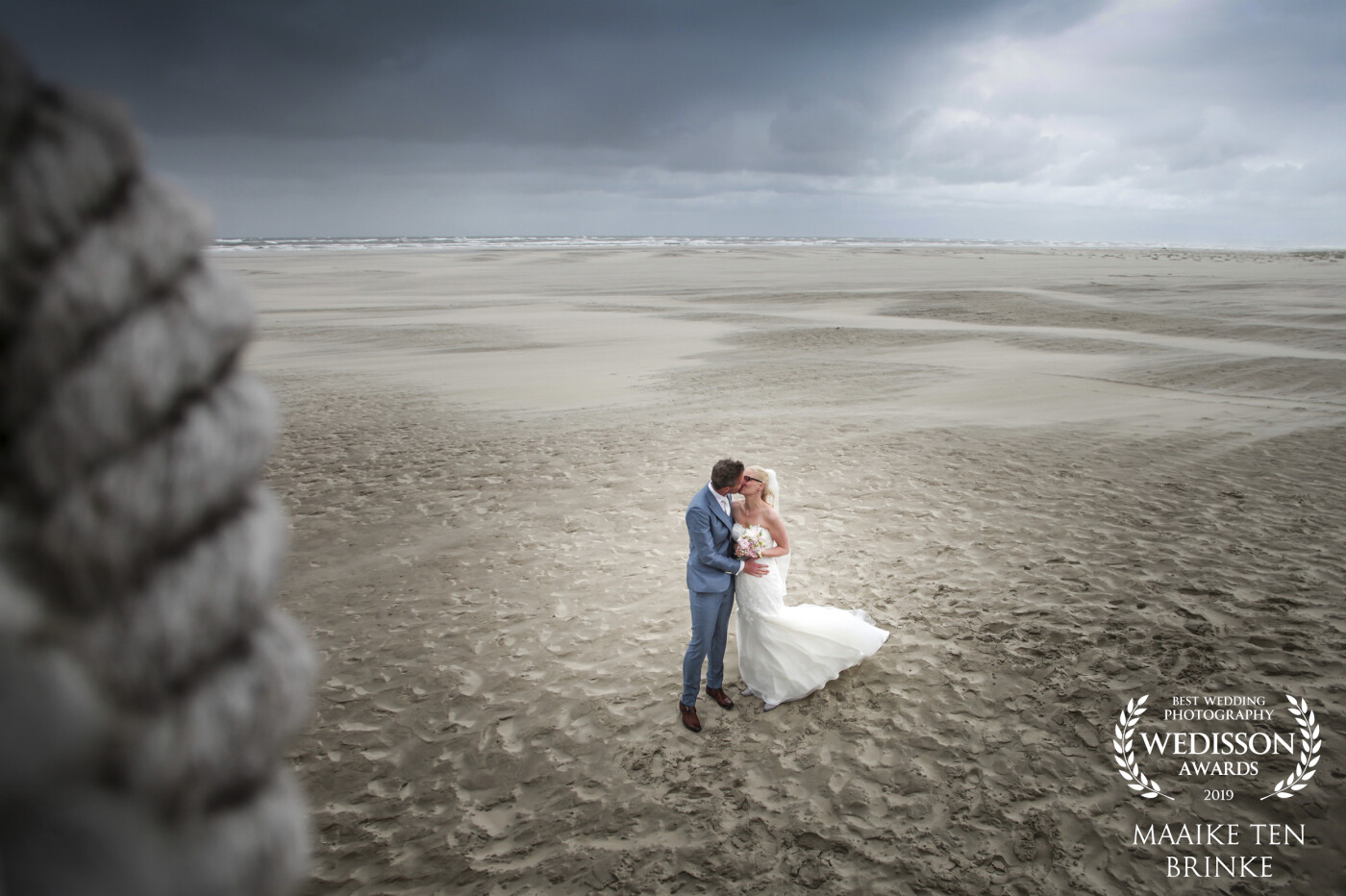 A stormy day in June on the lovely island Terschelling (Netherlands). With a wind force 10 it was a challenge to take pictures on the deserted beach. But we took the chance and made this lovely picture. <br />
Thanks, Wedisson for selecting this picture. Check out more of this couple on www.maaikefotografie.com
