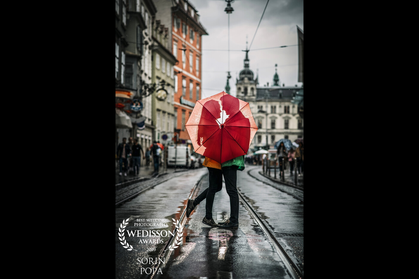 Shooting in bad weather seems to create amazing shoots! I shoot this picture on the streets of Graz, Austria! The couple was very playful, and they just stop to have a little hug, covering themselves with the umbrella. I chose to lit with a Speedlite flash to create some dramatic shadow. 