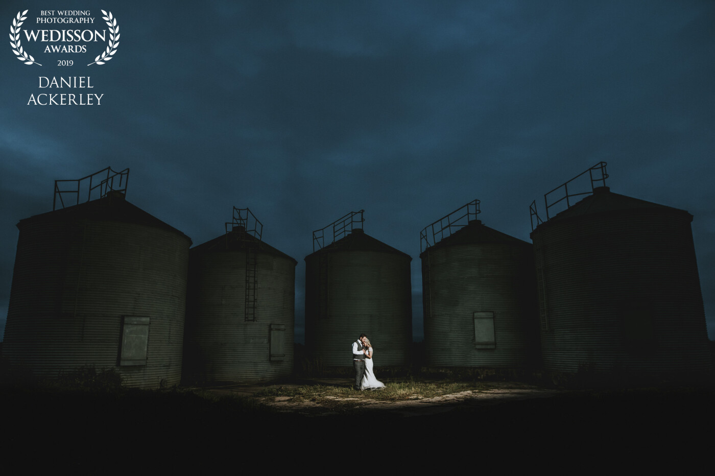 Cydney & Matt got married on an old farm, and these grain silos were just outside the main barn they were using next to the car park, and I thought they would make for an interesting back drop to a very moody and dark early evening sky. All of the light in the image was provided by a single MagMod MagBox, camera right, using a Nikon SB910 on 1/4th power. and this not only lit the couple perfectly but bounced light around the scene, providing some lovely soft front lighting on the silos. I simply edited out my assistant in PS to leave me with this final image.