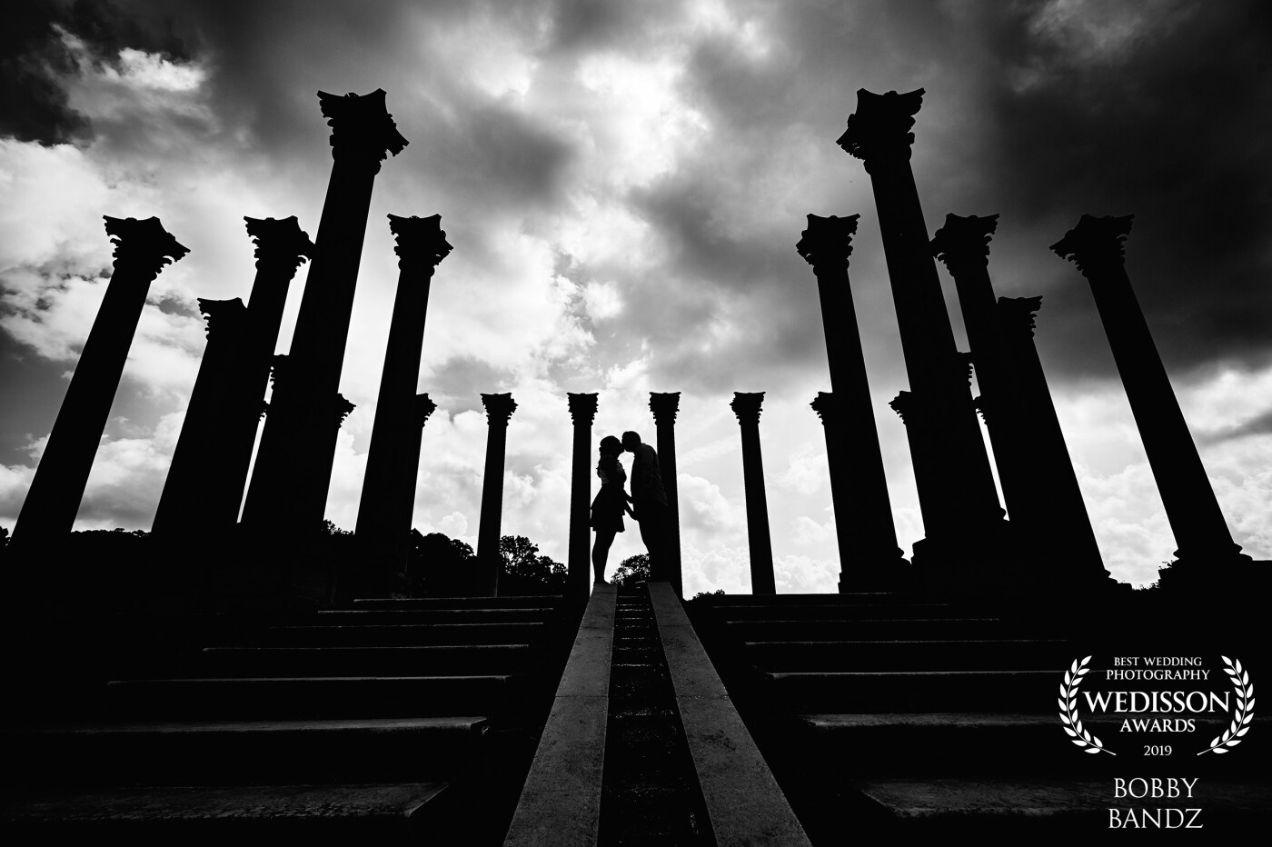 Sometimes people think the clouds aren't good for a photo session but in our case we love the elements because it tells the true story of the day! It was sunny and then the clouds rolled in so it was only fitting to make this photo a little more epic especially with the columns and that kiss!