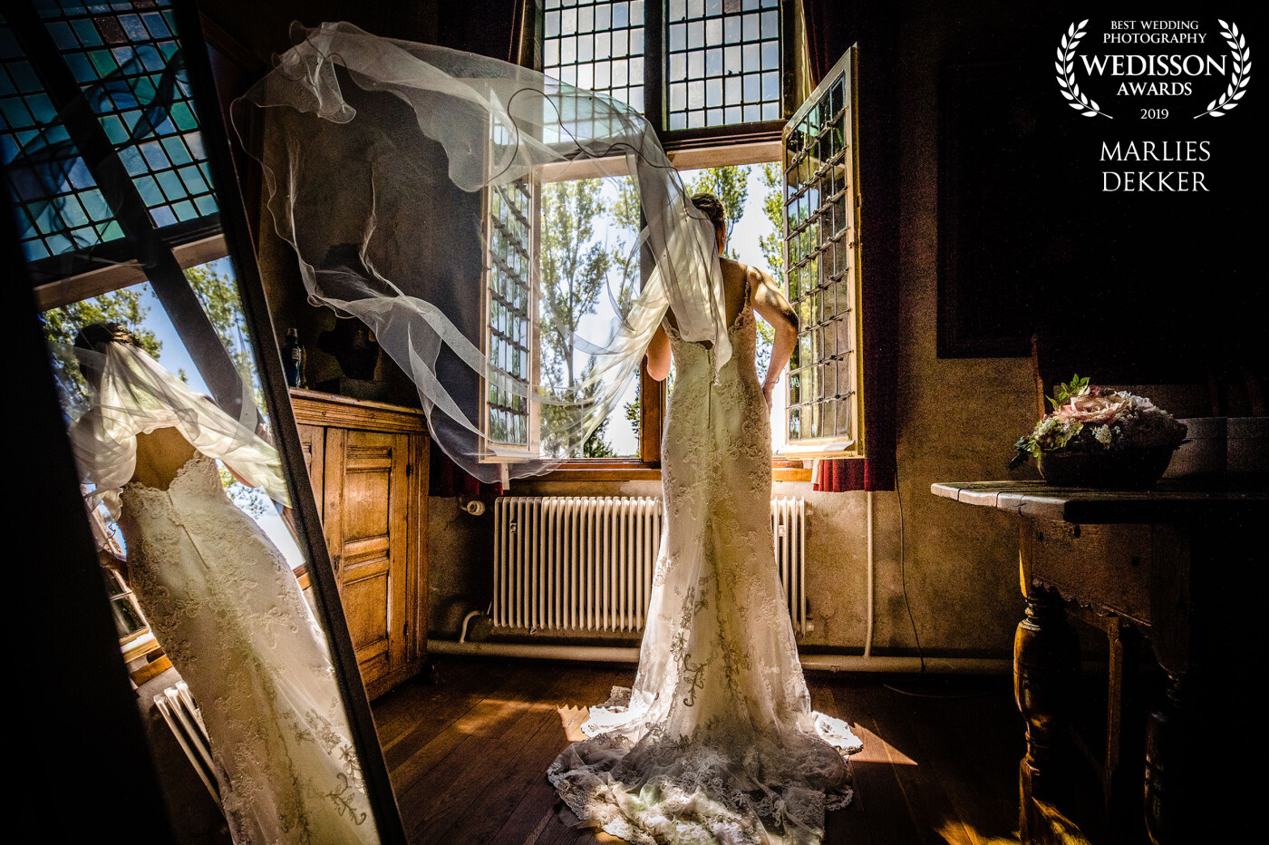 It was a very hot Dutch summer, which means when temperatures rise its most of the time quite hot and moisty. The Castle was warm as well and when the bride decided to open the window the wind came in to blow the veil away, the mirror did his own thing which made the scenery perfect for a shot like this.