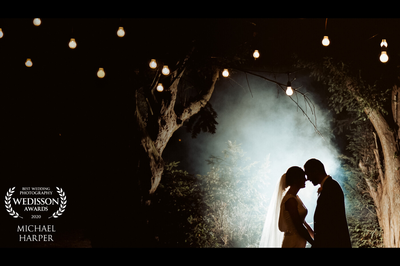 Captured at Wrenbury Hall at the end of the evening as their last photo. Using the hanging lights as an ambient feature a flash was positioned behind the couple to create a silhouette and light up the trees a little. To finish the scene white smoke was introduced to add some drama to the image.