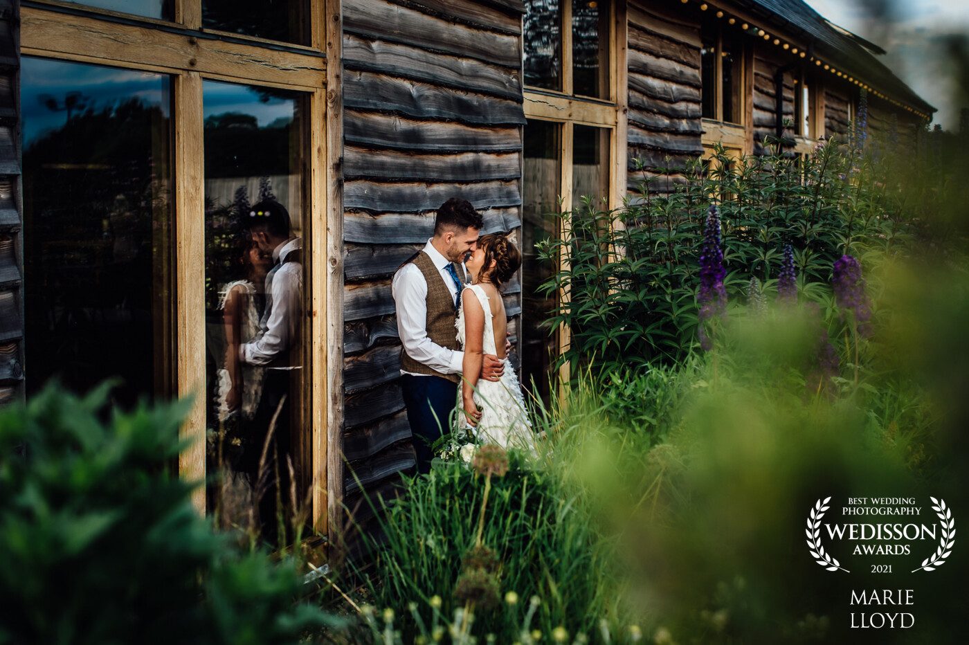 Summer wedding in a Welsh Oak barn conversion in North Wales, with the bride and groom in evening light placed next to a window for a reflection and I used the planting for the foreground to frame it.