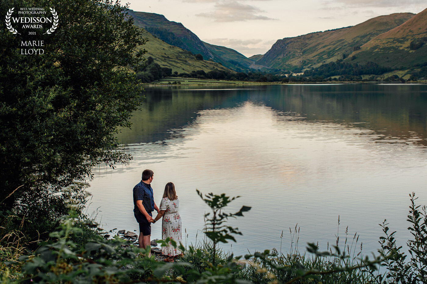 Couple looking out over the reservoir, the light is fading and creating a lovely leading line across the water, with the foliage creating a delicate frame for the couple.
