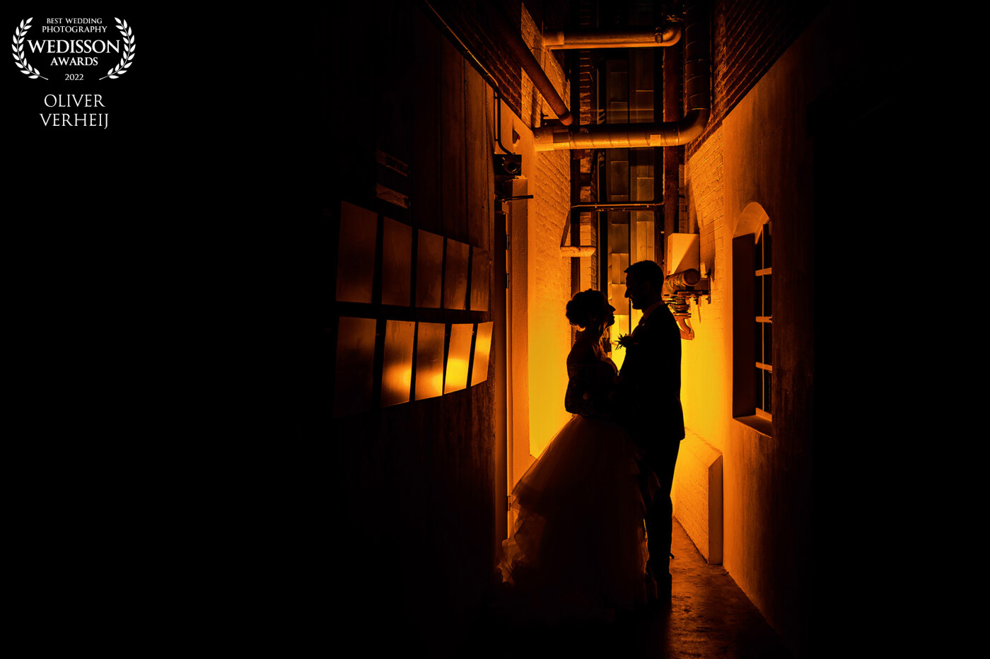 This photo was shot at their wedding location at the DRU Cultuurfabriek in Ulft. I decided to put a flash with an orange filter behind the couple to create this amazing atmosphere. The couple loved this image because they wanted to some special shots with an industrial touch.