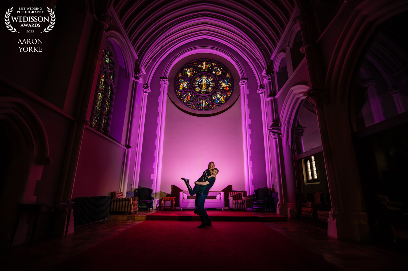 I took this shot at the beautiful Stanbrook Abbey in Worcestershire. It was an engagement shoot for a couple getting married there. I wanted to light the back wall up with a purple/pink colour so to do this I placed a bare flash full power with a gel facing the wall. I then placed a grid on a front flash from the side and lit the couple. The rest was all down to Paul (the groom) to do the lovers lift and to hold Angela (the bride) in position to get the shot! So much fun to take!