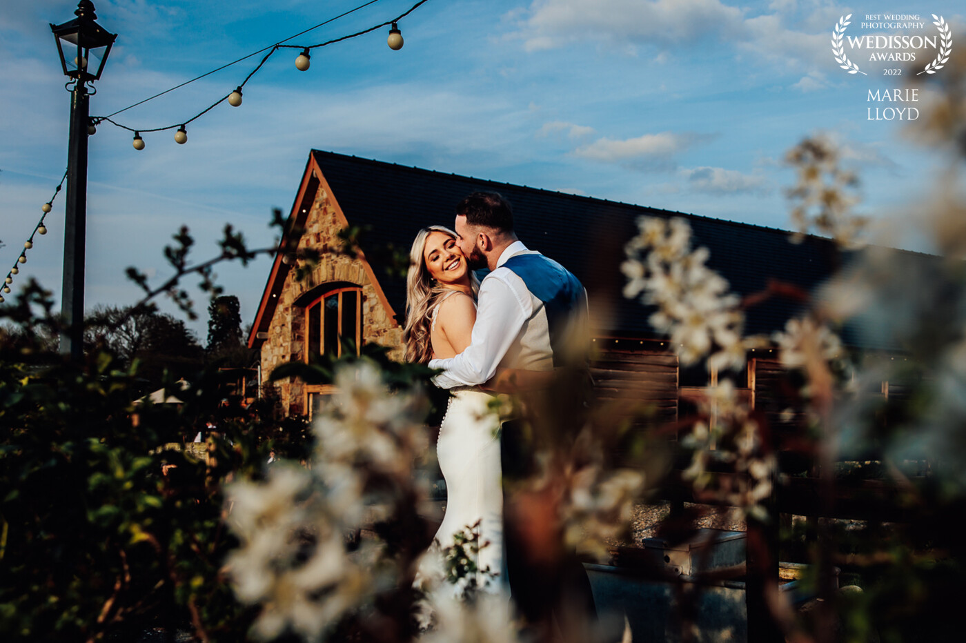Photographed in the golden evening light at a barn wedding. The foliage and flowers were used as a foreground frame and the roof as a lead in line and frame. It was shot at a low angle.