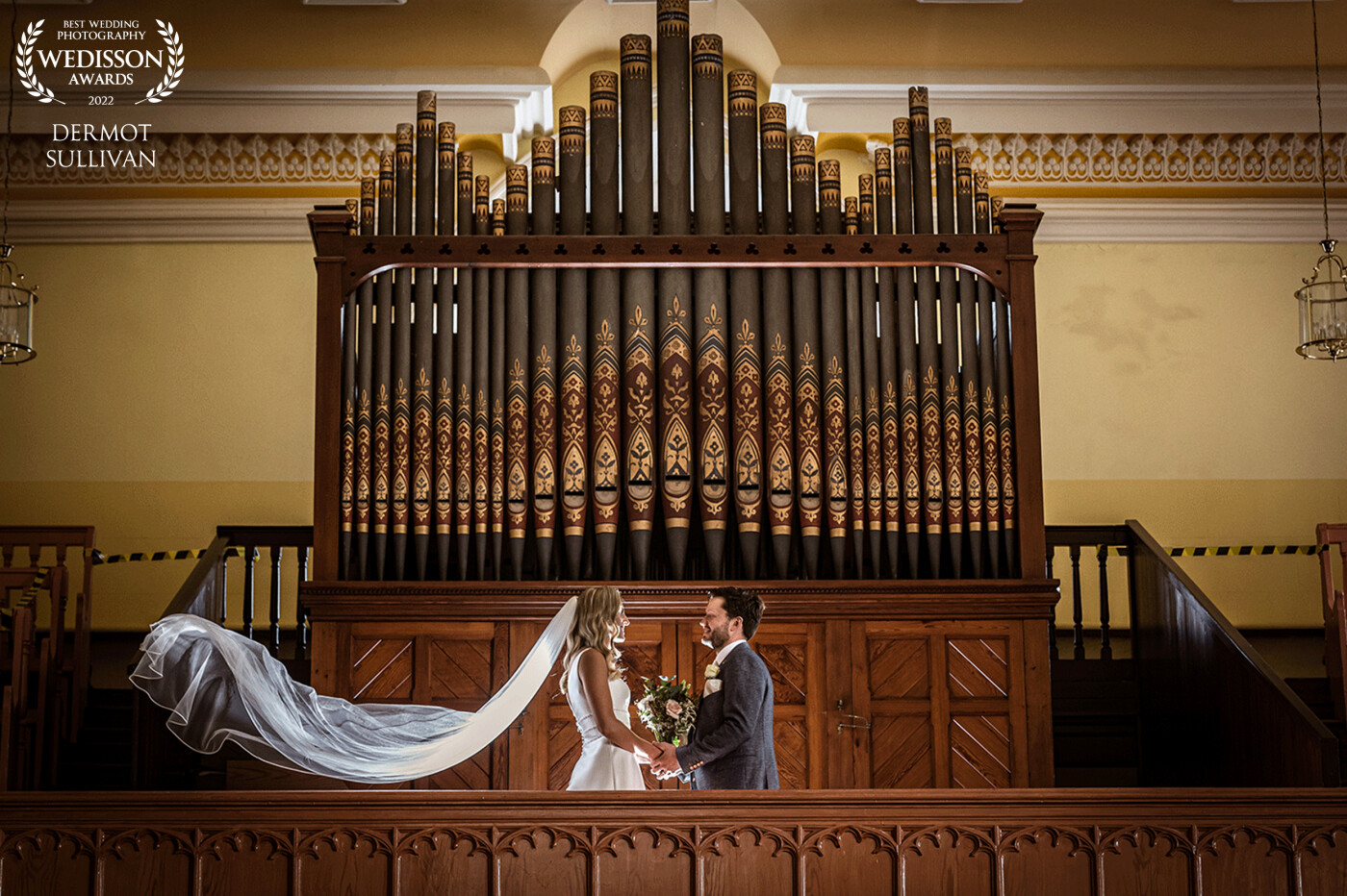 I spotted the organ loft during the ceremony and thought that it would be a great background for a couple shot. The bride and groom were up for a creative photograph, so I positioned a remote flash behind them and got the brides younger brother to flick the veil and then quickly duck down, It took a couple of tries, but we got the photo!